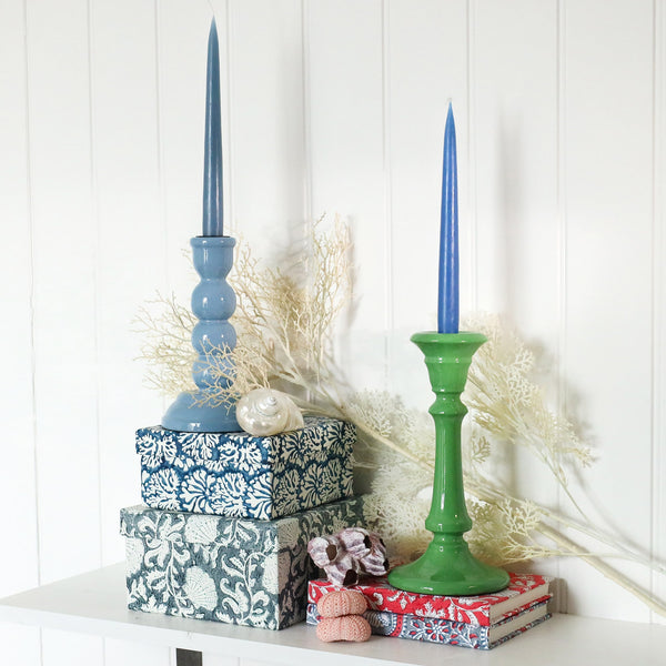 Powder Blue candle holder placed on a couple of hand painted boxes.Next to this is another candle holder placed on a couple of hand blocked painted notebooks.Both have candles in them,there are shells also in the picture