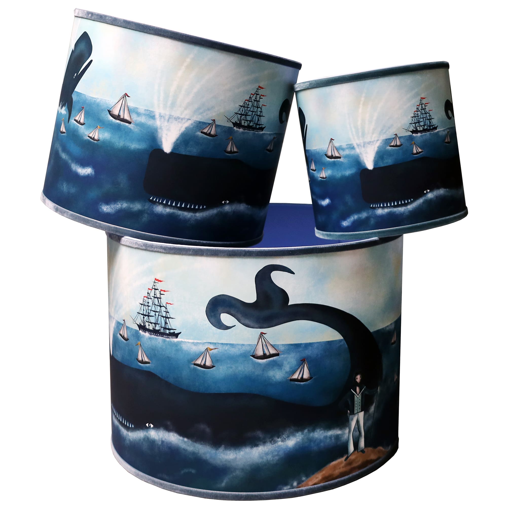 Three stacked drum-shaped lampshades featuring a nautical design inspired by classic maritime adventures. The artwork depicts large whales spouting water as they swim among sailboats and a tall ship with red sails. A captain stands on a rocky shore in the lower corner, gazing out at the scene, while a whale’s tail arches dramatically out of the water. The deep blue hues of the ocean and sky create a sense of adventure and exploration. The lampshades vary in size, showcasing the same vivid design that evokes