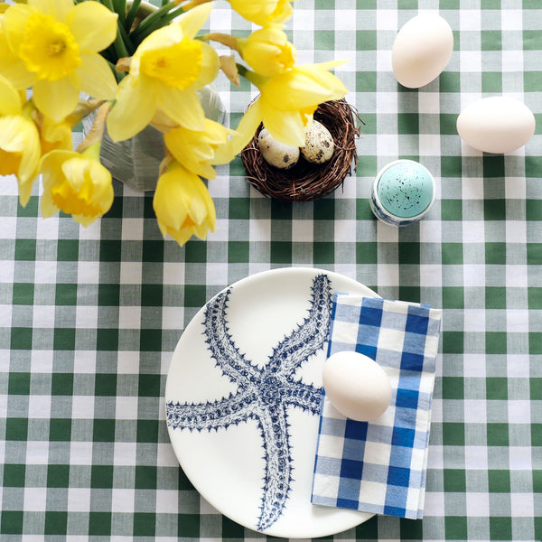 Bone China White dinner  plate with hand drawn illustration of a starfish in navy. There is a folded blue gingham napkin with a duck egg on the plate. The table is laid for Easter with a green gingham tablecloth, eggs and daffodils.
