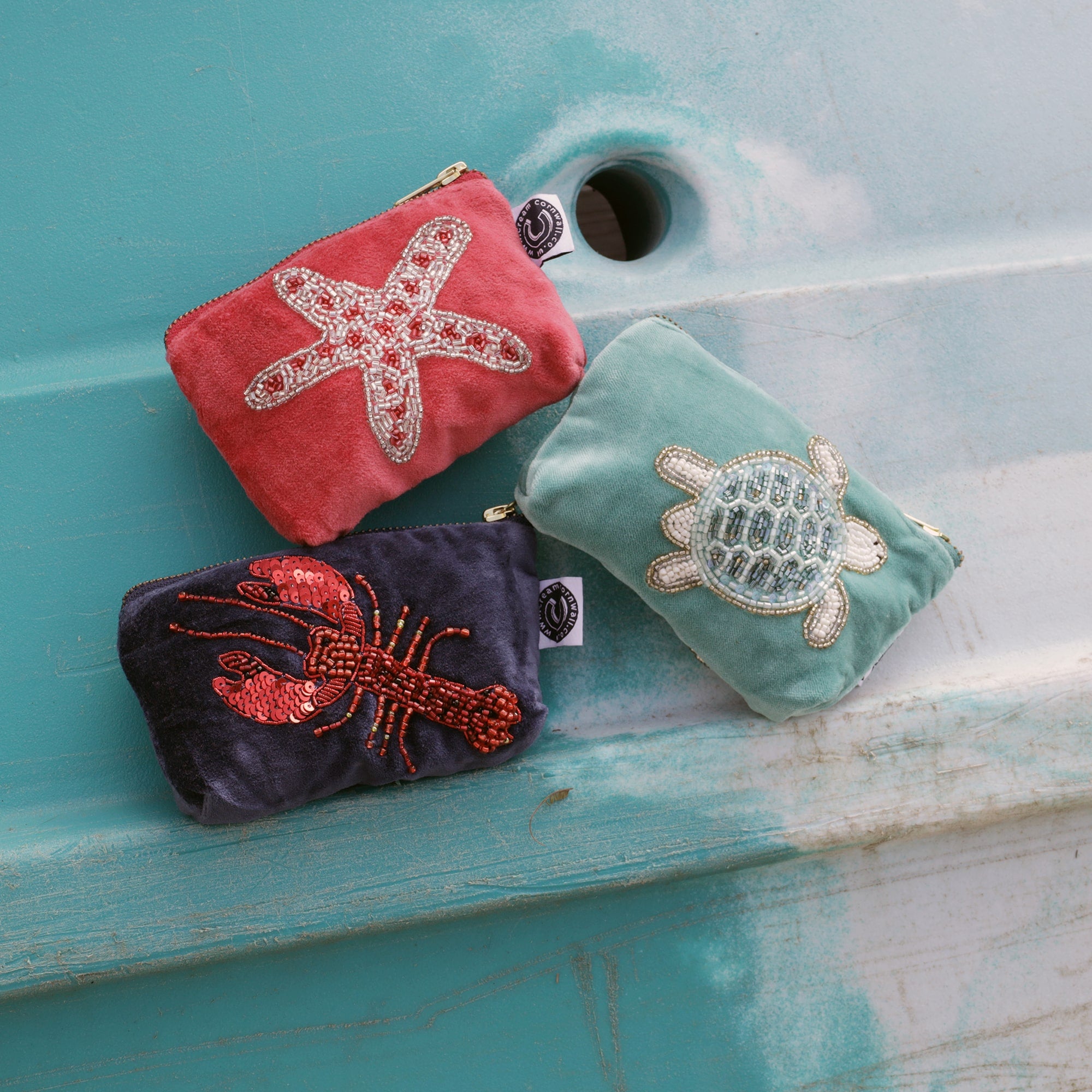 3 velvet beaded coin purses balanced on a turquoise surf board, on with w lobster, one with a starfish and one with a turtle on.