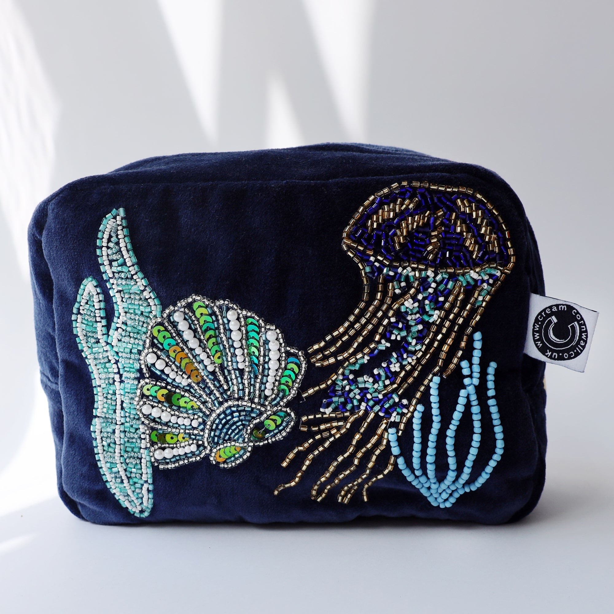 Beaded velvet cosmetic bag featuring an intricate design of a jellyfish and seashell, made with beads and sequins in shades of blue, gold, and green, resting against a dark navy background