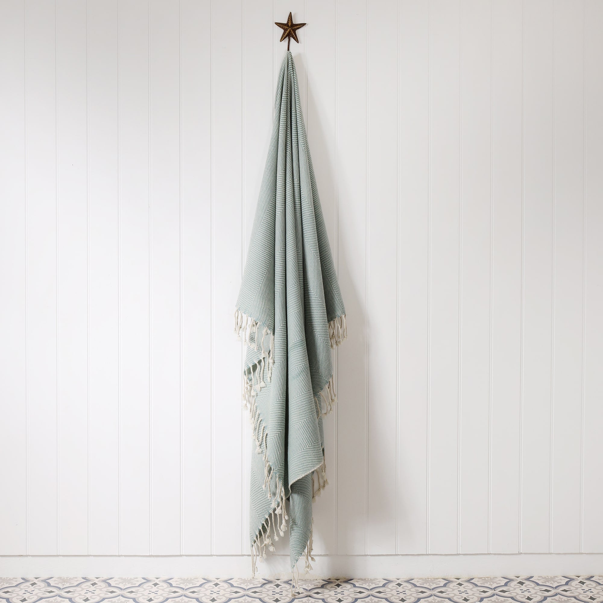duck egg and cream woven throw with knotted fringe hanging on a brass starfish hook against a white tongue & groove wall