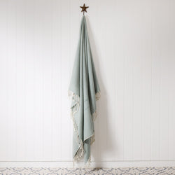 duck egg and cream woven throw with knotted fringe hanging on a brass starfish hook against a white tongue & groove wall