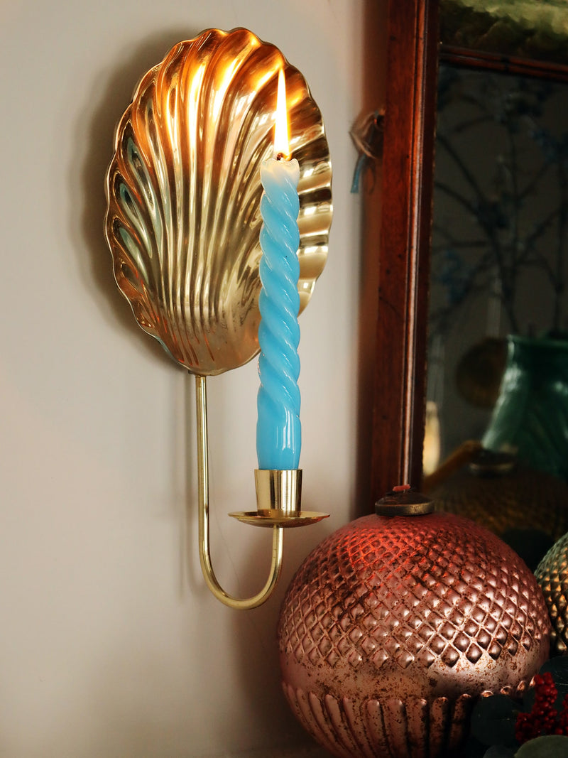 scallop shell brass wall scone with lit twisted blue candle above a mantlepiece with winter foliage and large glass baubles