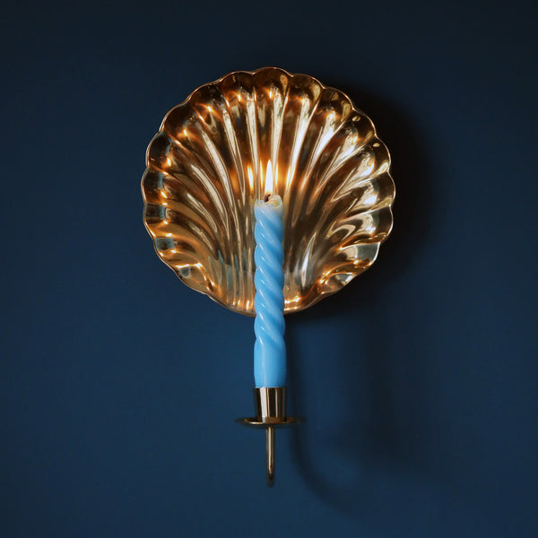 scallop shell brass wall scone with pale blue twisted lit candle on a dark teal background