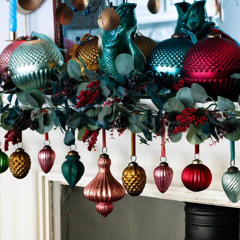 vintage inspired coloured glass baubles hanging from a mantlepiece with winter foliage