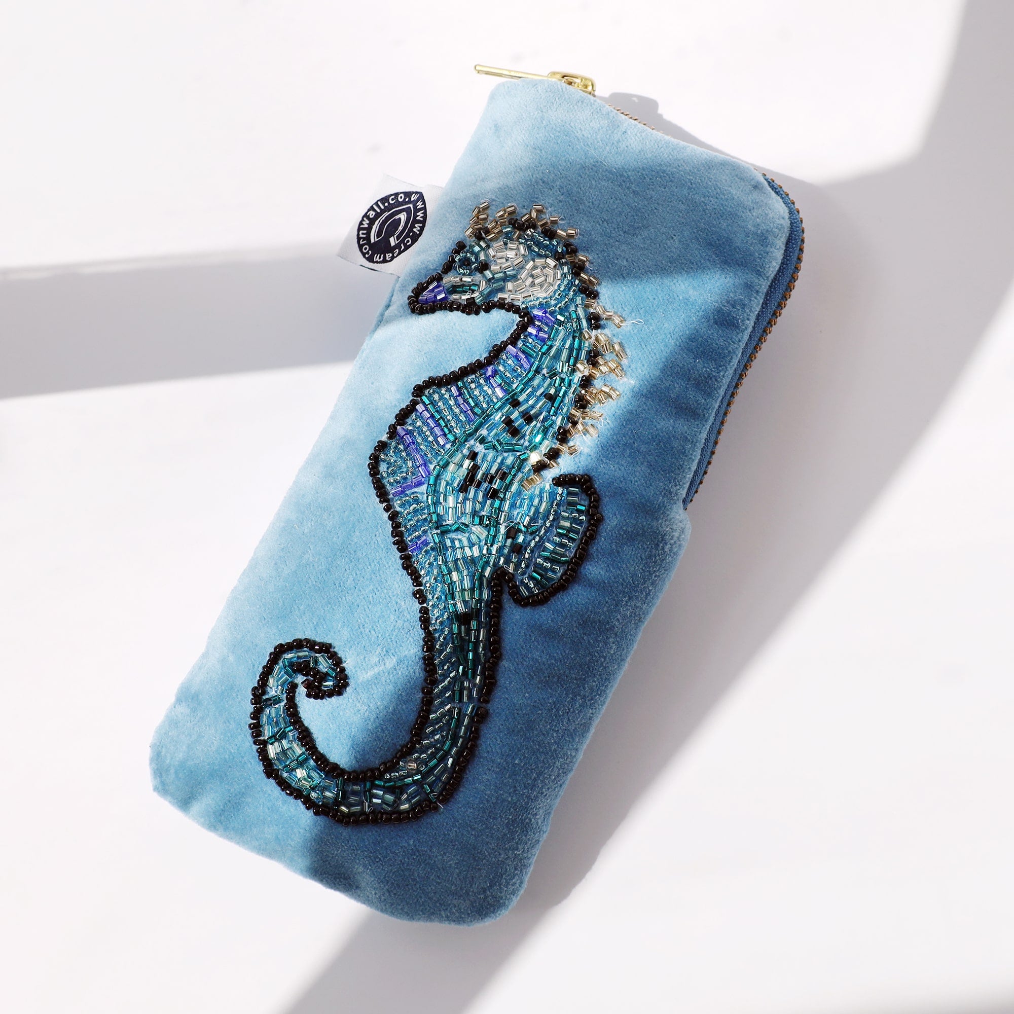 Light blue velvet glasses case beaded seahorse decoration on the front on a white background with the sun casting shadows across it.