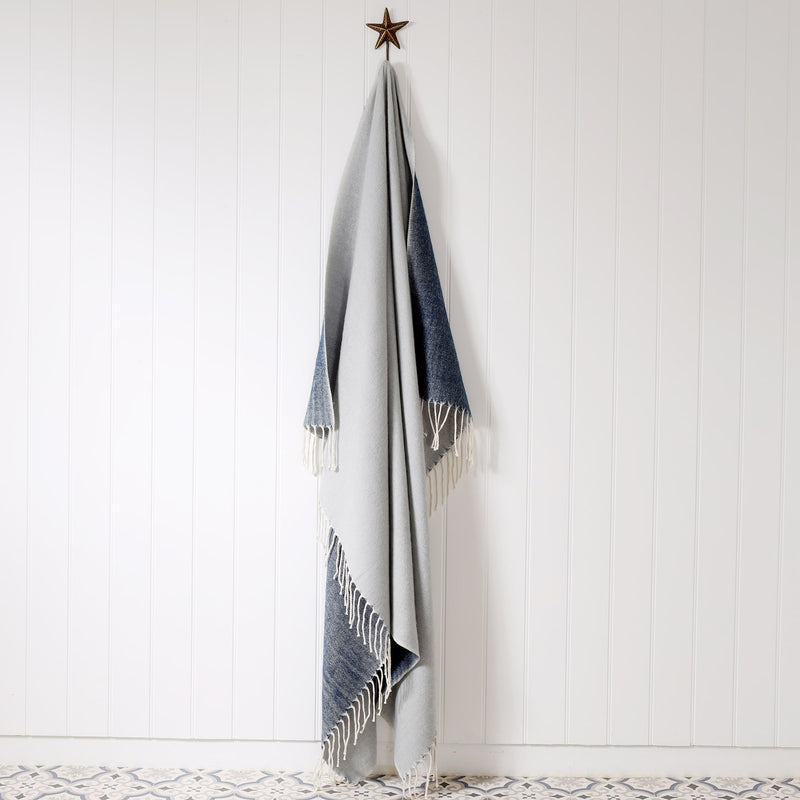 grey and navy  reversible brushed throw hanging on a brass starfish hook against a white tongue & groove wall