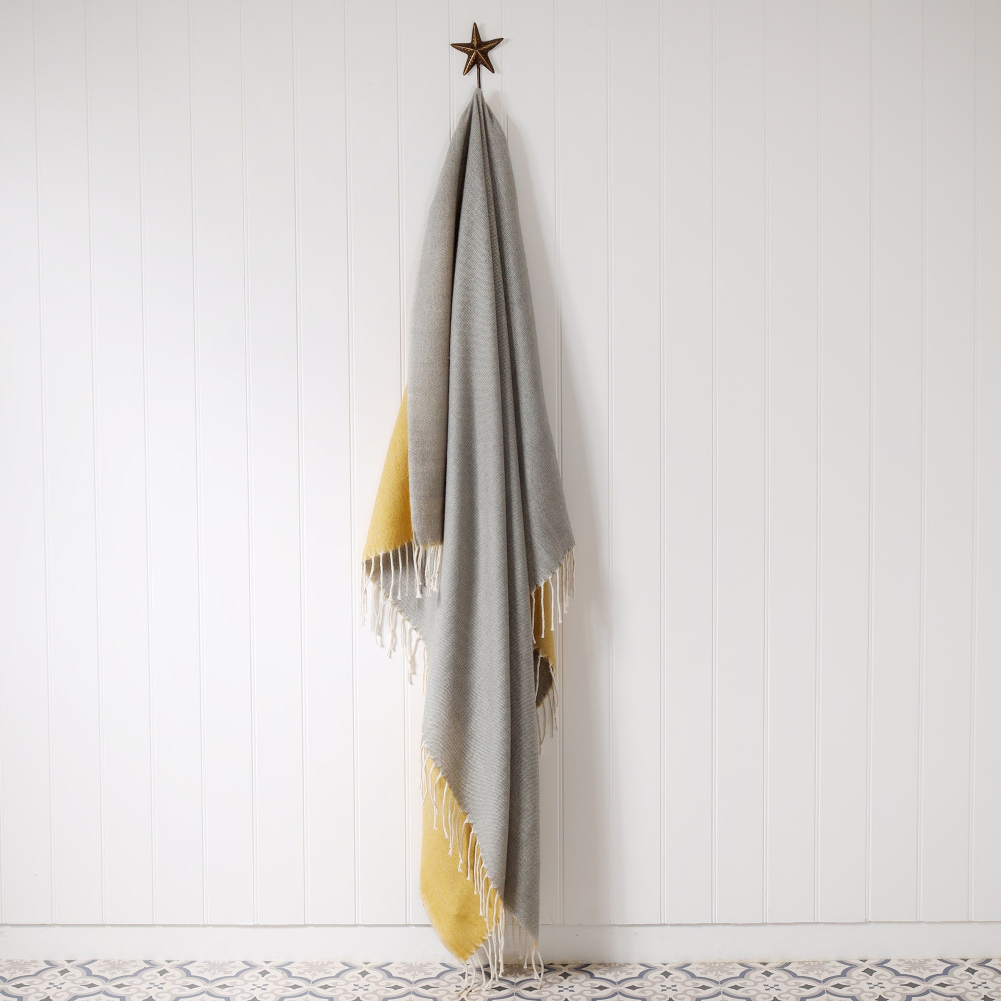 reversible grey and mustard  reversible brushed throw hanging on brass starfish hook on a white tongue & groove wall