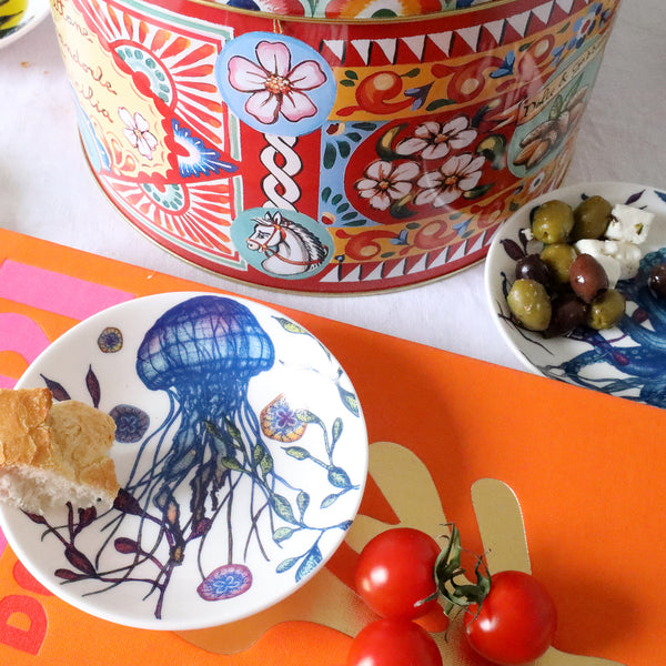 Nibbles bowl in Bone China in our colourful Reef range in the Jellyfish design placed on a brightly coloured book.Next to it is a brightly coloured large tin and another reef nibbles bowl with olives