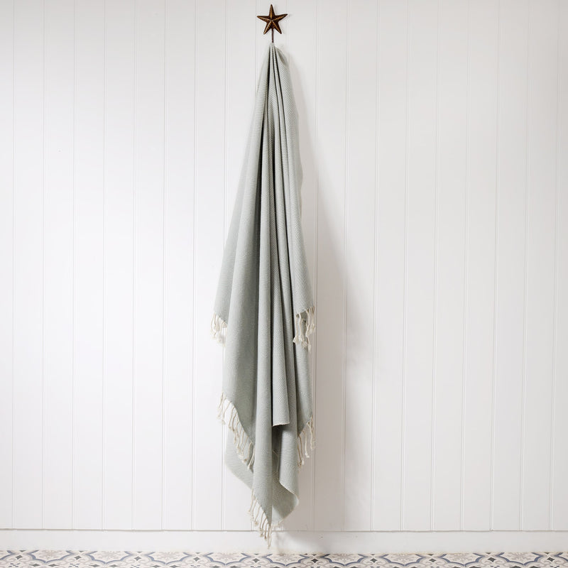 light grey and cream herringbone throw hanging on a brass starfish hook on a white tongue & groove wall