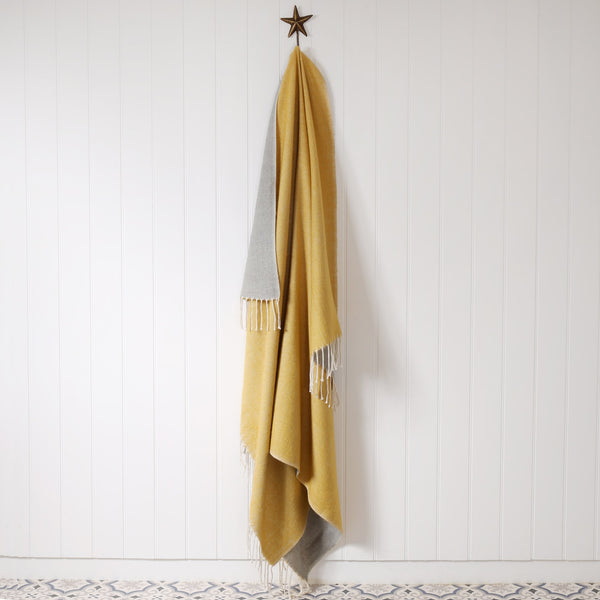 reversible mustard and grey reversible brushed throw hanging on brass starfish hook on a white tongue & groove wall