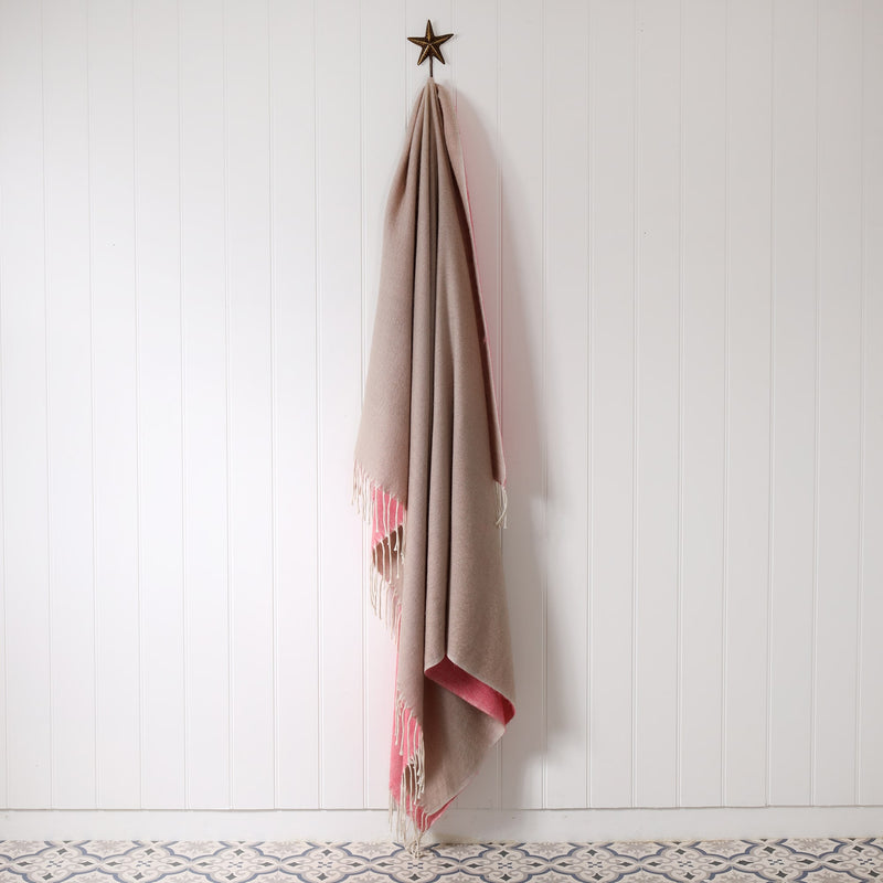 natural and pink brushed throw hanging on a brass starfish hook against a white tongue & groove wall