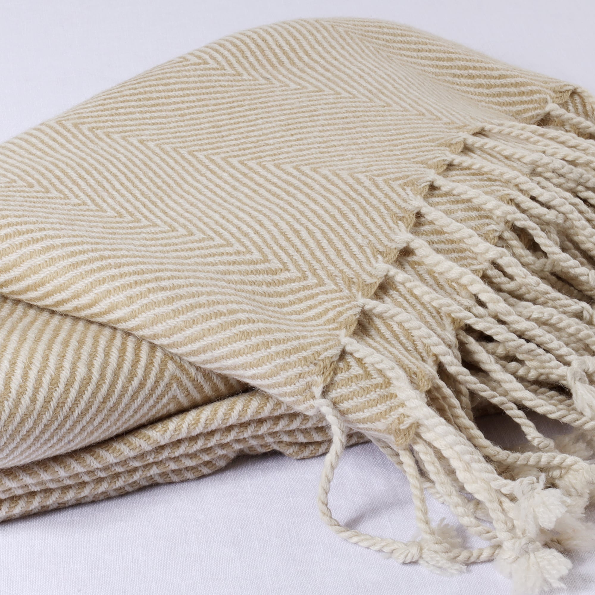 folded natural herringbone throw on a white background showing the weave detail and the knotted cream tassle edge