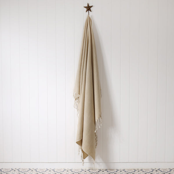 natural & cream herringbone throw hanging on a brass starfish hook against a white tongue and groove wall