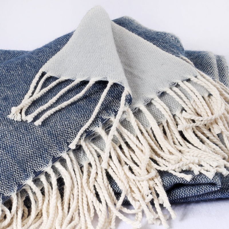 folded navy and grey reversible brushed throw on a white background to show the weave and twisted fringe details