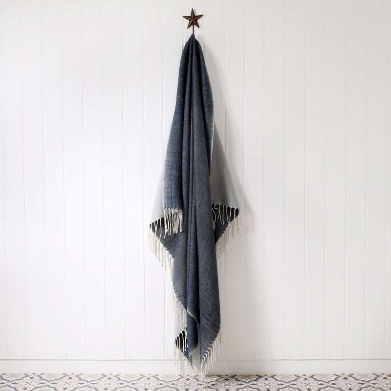 navy and grey reversible brushed throw hanging on a brass starfish hook against a white tongue & groove wall