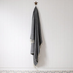 navy and cream herringbone throw hanging on a brass starfish hook against a white tongue & groove wall