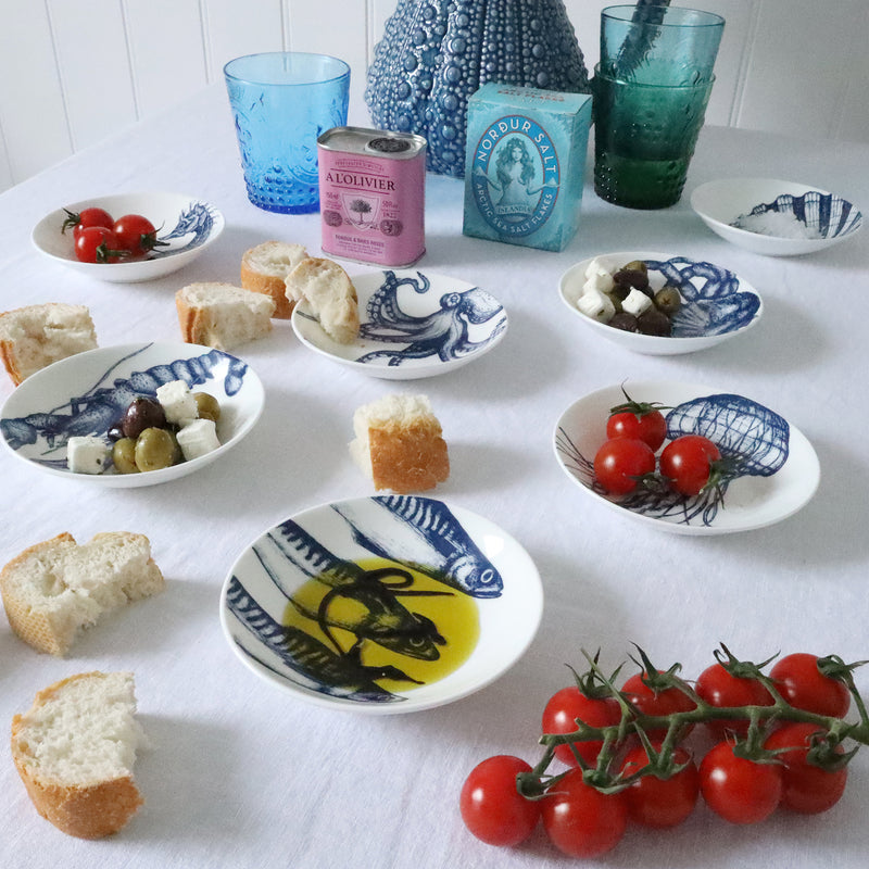 Nibbles bowl in Bone China in our Classic range in Navy and white in the Jellyfish design placed on a  white table cloth are more nibbles bowls with various foodstuffs in,in the background is a large blue jug and colourful glasses
