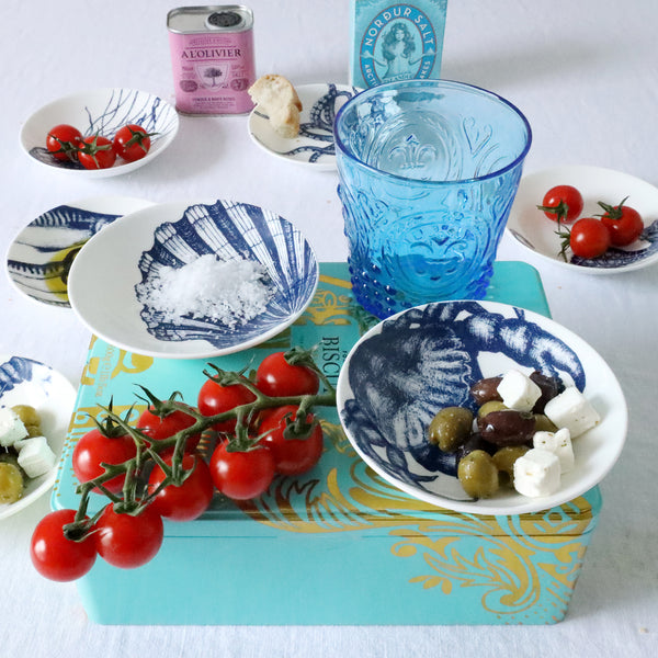 Nibbles bowl in Bone China in our Classic range in Navy and white in the Scallop design placed on a turquoise box filled with salt.Also on the box is a crab nibbles dish with some olives in .On the table below on a white table cloth are more nibbles bowls with various foodstuffs in