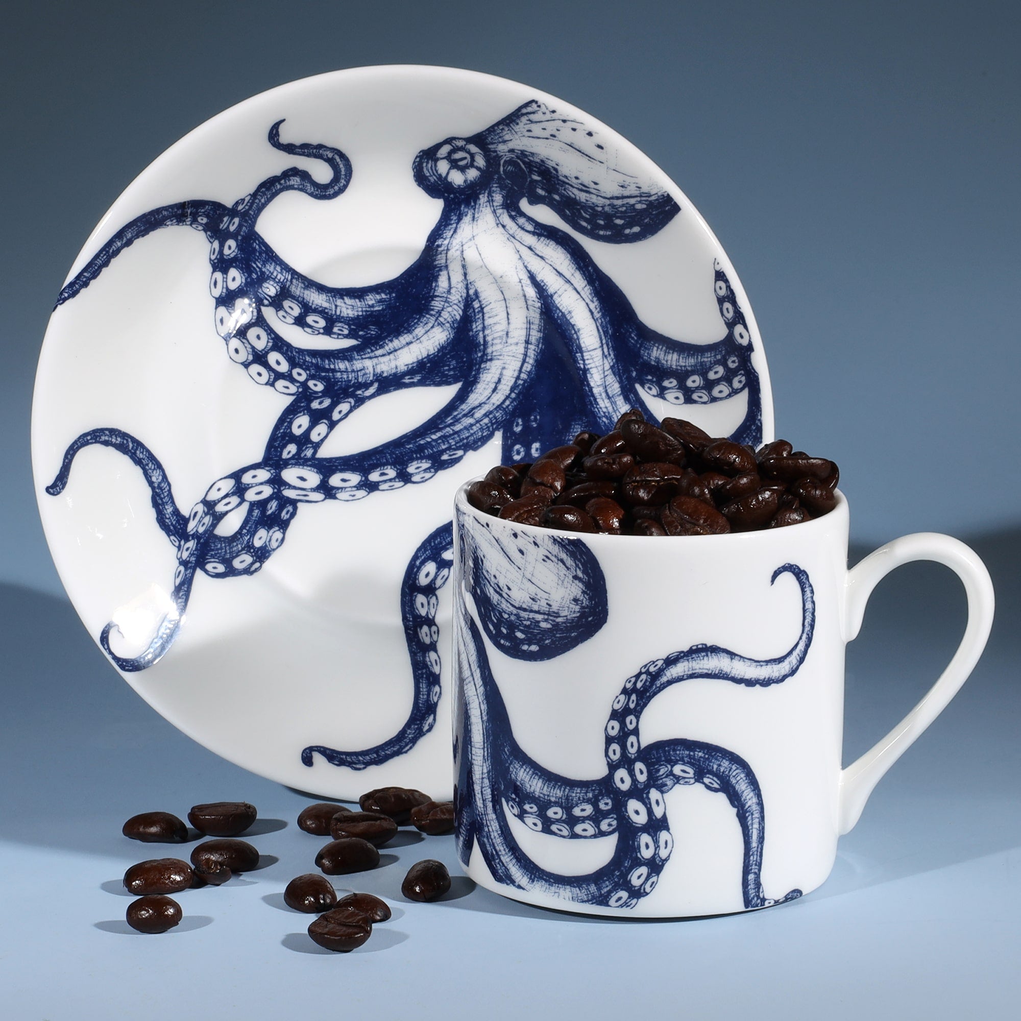 Bone China white espresso cup in hand drawn illustration in our Octopus design in Navy with matching saucer.Saucer is standing on its side with the coffee cup in front filled with coffee beans