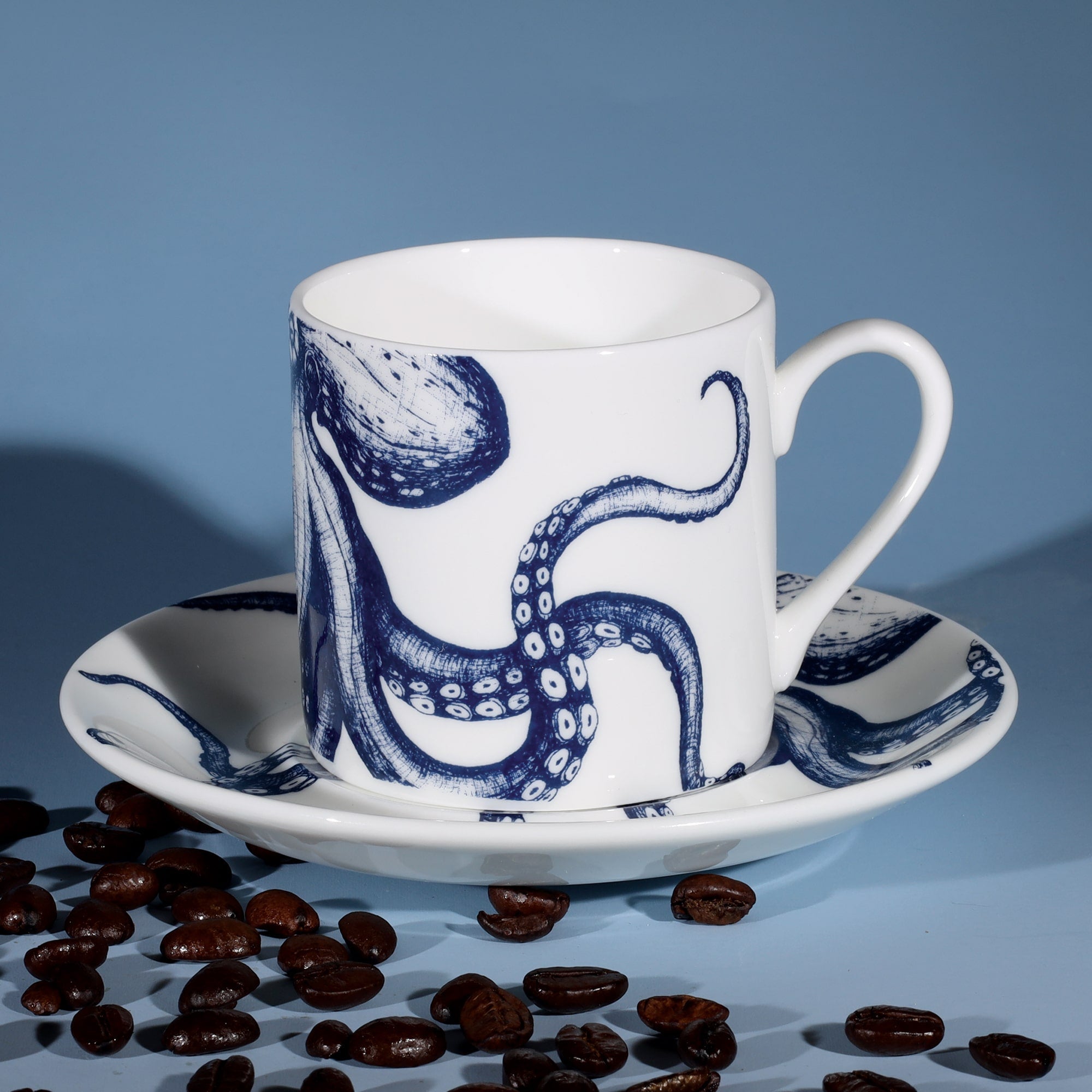 Bone China white espresso cup in hand drawn illustration in our Octopus design in Navy with matching saucer surrounded by coffee beans