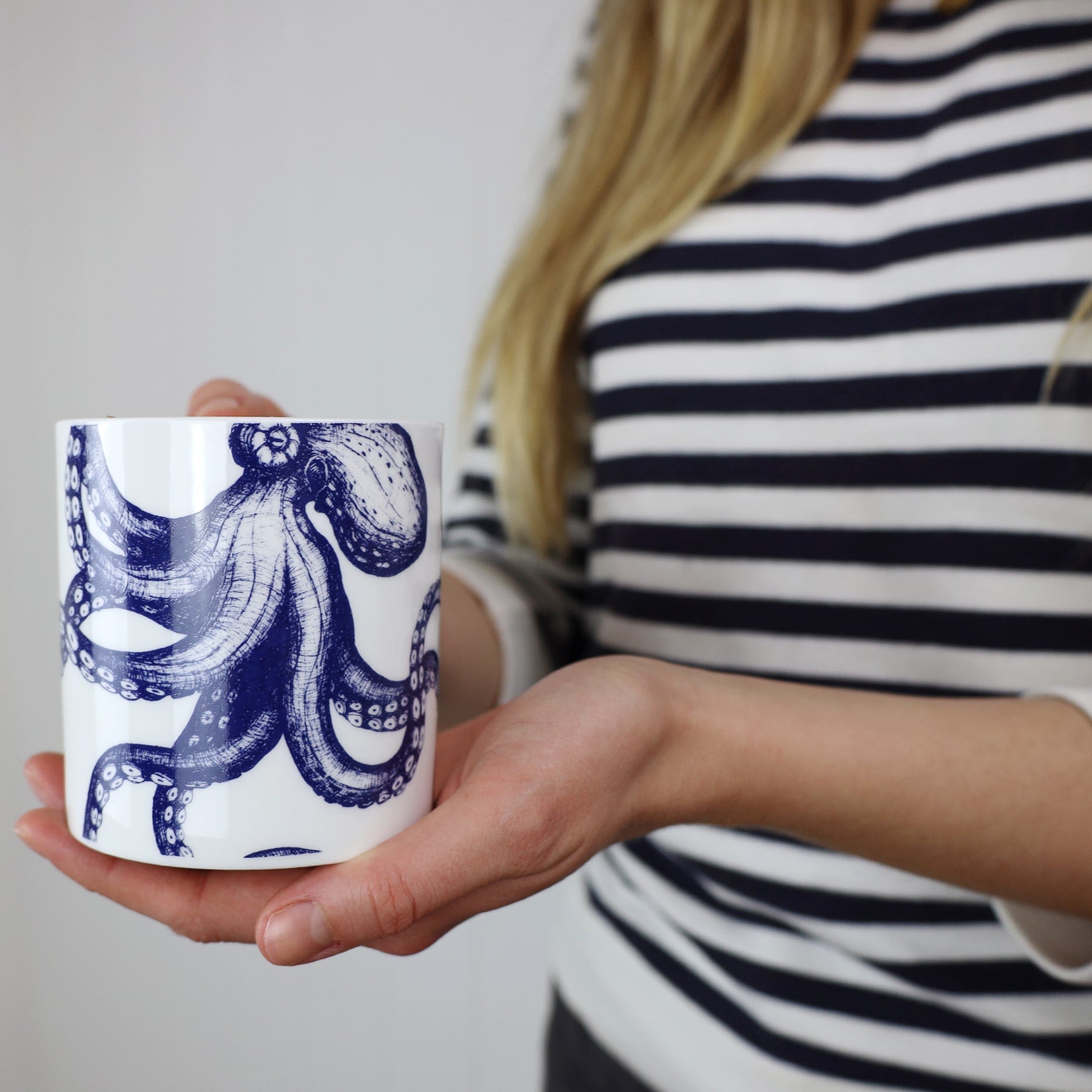 The photo shows Bone china mug featuring a hand drawn octopus design in classic blue and white being held by a woman