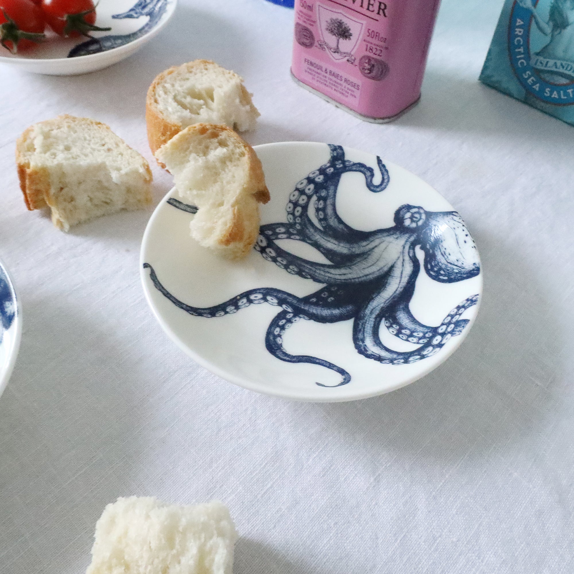 Nibbles bowl in Bone China in our Classic range in Navy and white in the Octopus design placed on a white table cloth with bits of French stick on the table