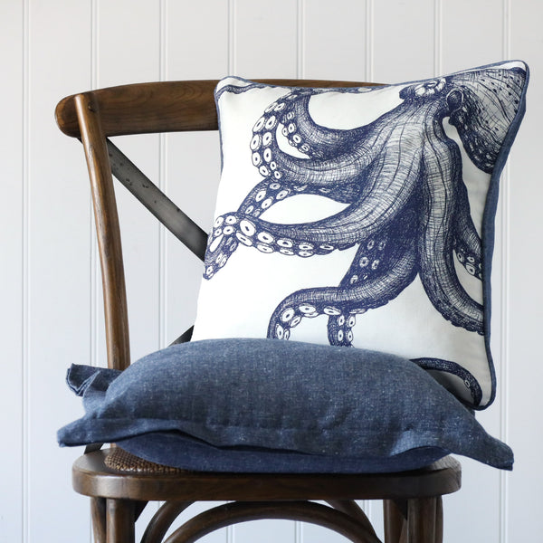white cushion with navy illustrated octopus on the front, placed on a linen cushion on a wooden chair