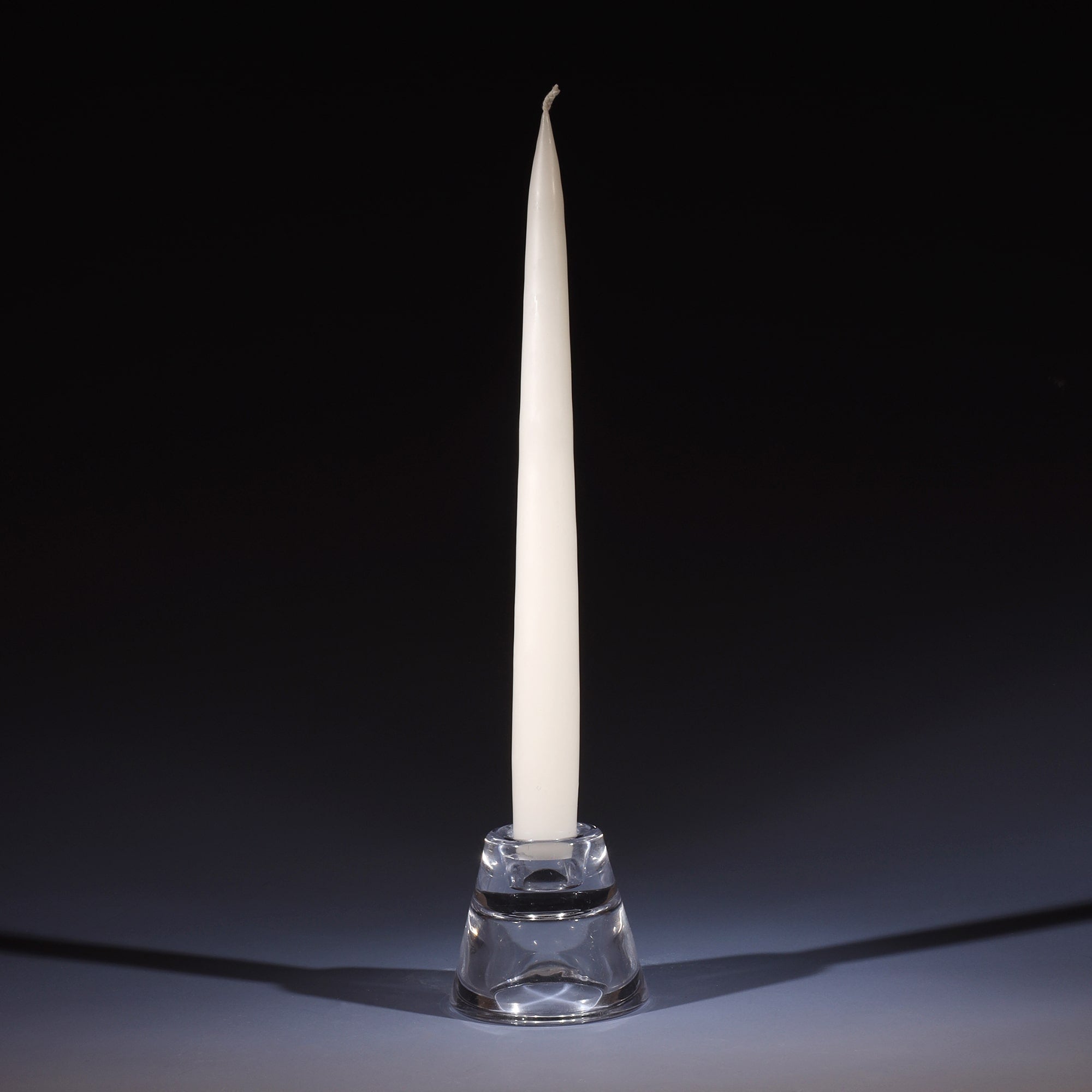 off white tapered dinner candle in a small glass candle holder on an ombre blue background