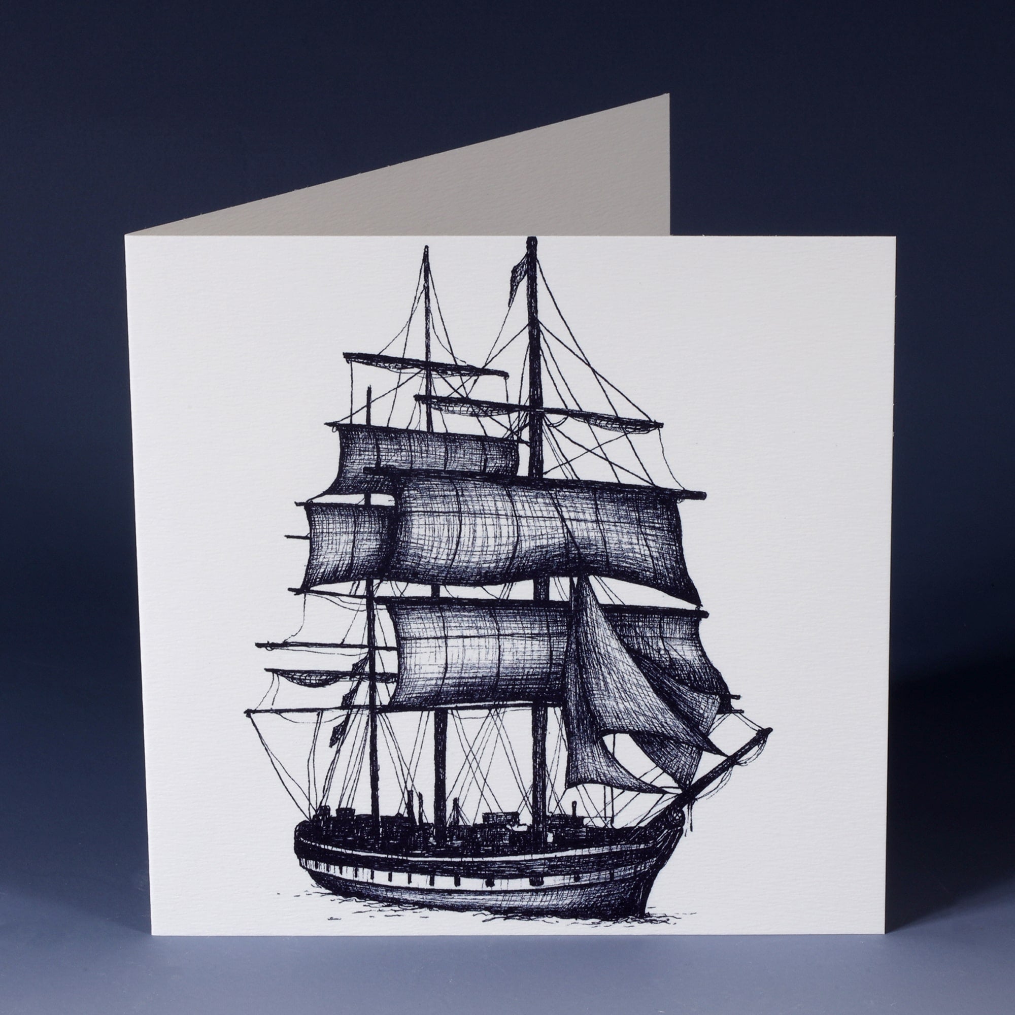 front of a white greeting card with a navy illustrated packet ship sailing forwards sitting on an ombre blue background