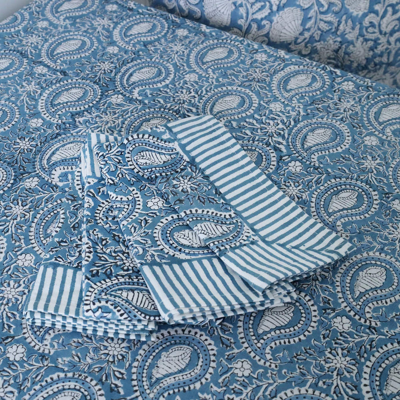 Azure Paisley Shell tablecloth which is a Hand block printed fabric in a soft blue paisley print.Placed on the tablecloth are four matching napkins.