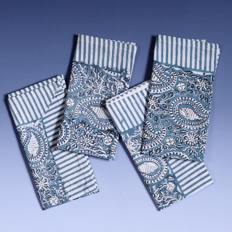 Azure Paisley Shell napkins which are Hand block printed fabric in a soft blue, the print is a repeat paisley with a shell theme throughout with swirling flowers, blue striped finished edge.There are four on top of each other in a line.