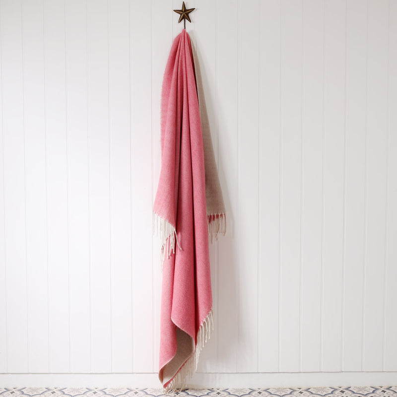pink and natural brushed throw hanging on a brass starfish hook against a white tongue & groove wall