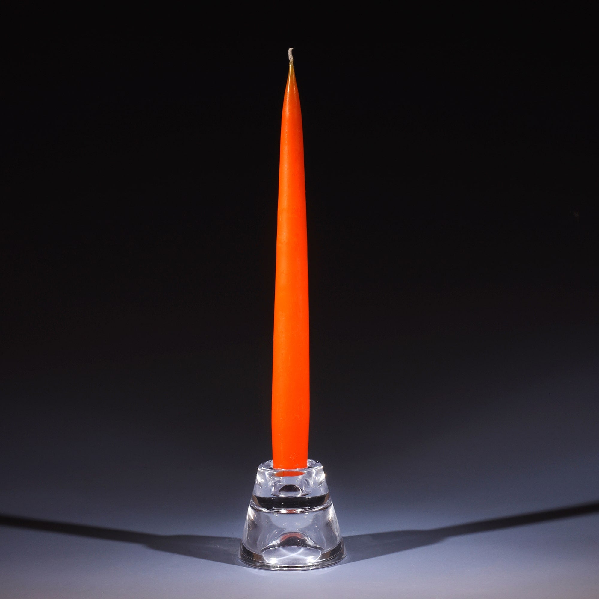 burnt orange tapered dinner candle in a small glass candle holder on an ombre blue background