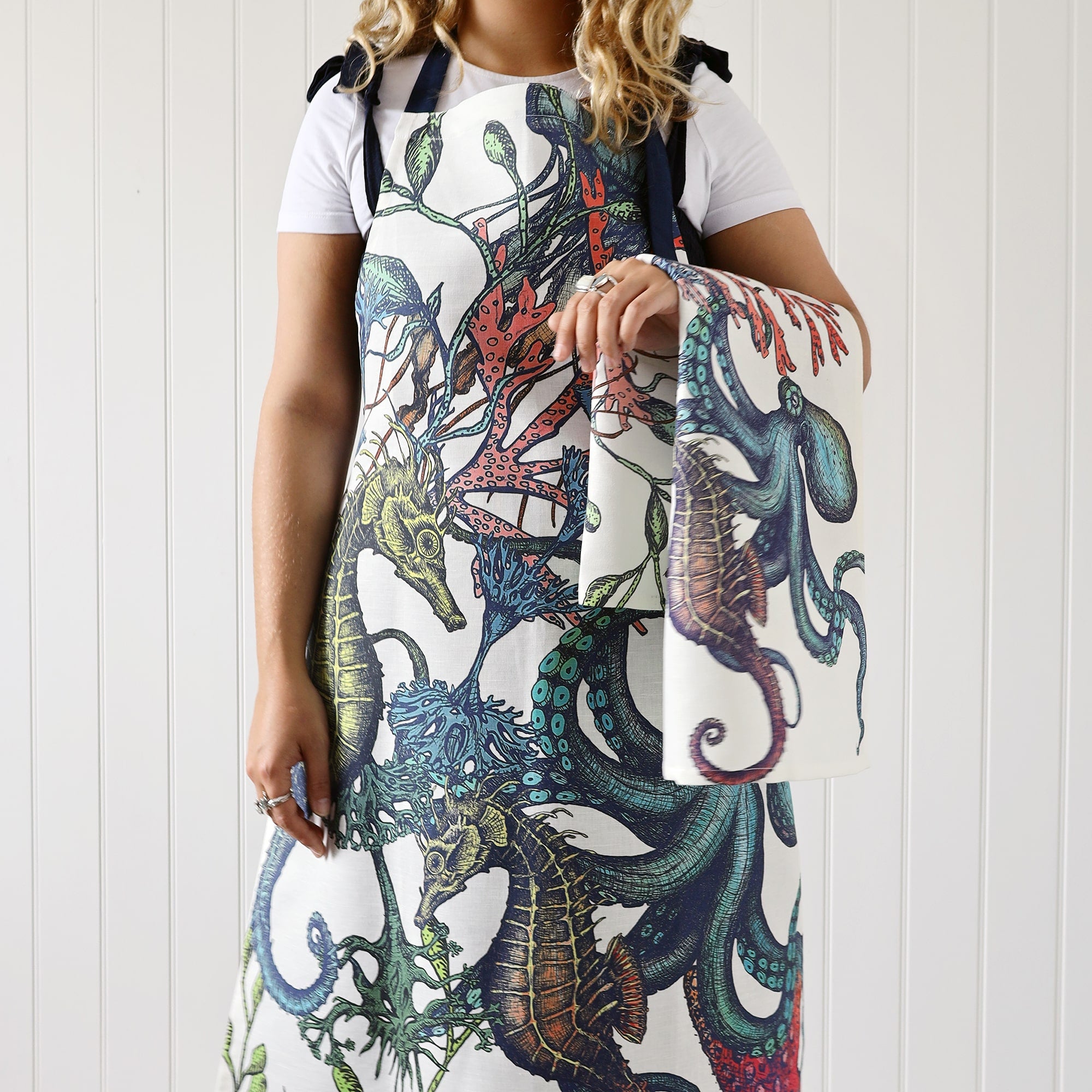 Our reef apron being worn by a model who is also holding a beachcomber tea towel over her arm