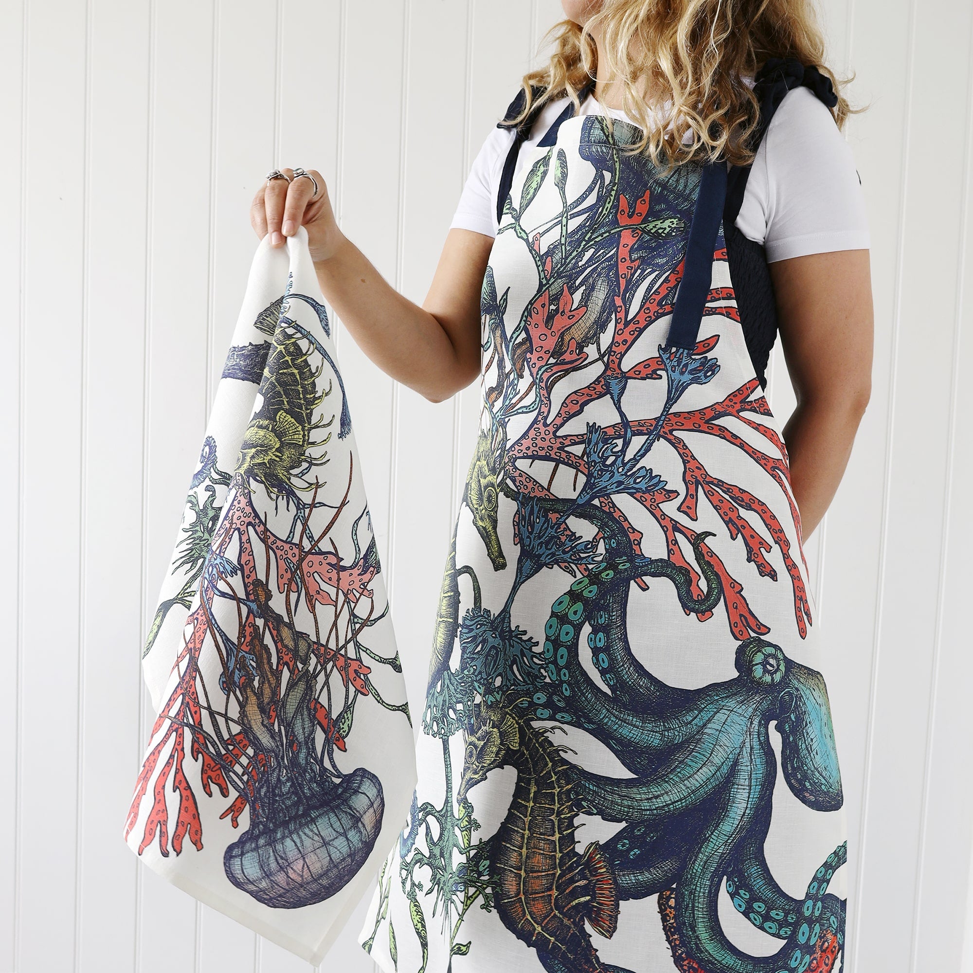 Our reef apron being worn by a model who is also holding a reef tea towel