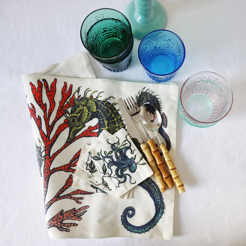 Fabric coasters in our Reef design in a set of four,placed on the matching placemats,they are folded over.Also on the table are bamboo cutlery and some coloured glasses