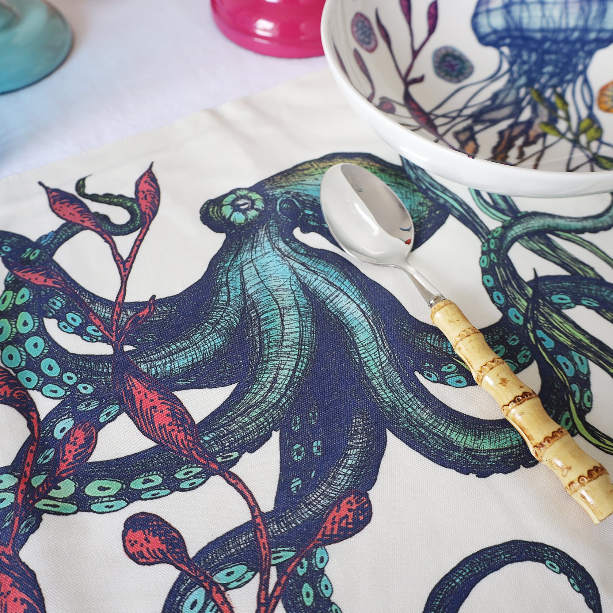 Close up of Reef design showing an octopus  placed next to a matching coaster on a tablecloth with Bamboo cutlery