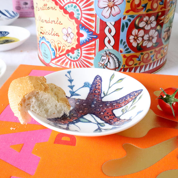 Nibbles bowl in Bone China in our colourful Reef range in the Jellyfish design placed on a brightly coloured book.Next to it is a brightly coloured large tin 