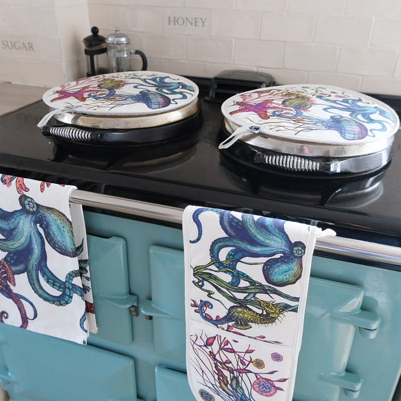 Cotton and Linen mix Tea Towels with hand drawn illustrations in Reef design draped over the arm of a green aga in a kitchen.On the top of the Aga are matching Reef Aga covers