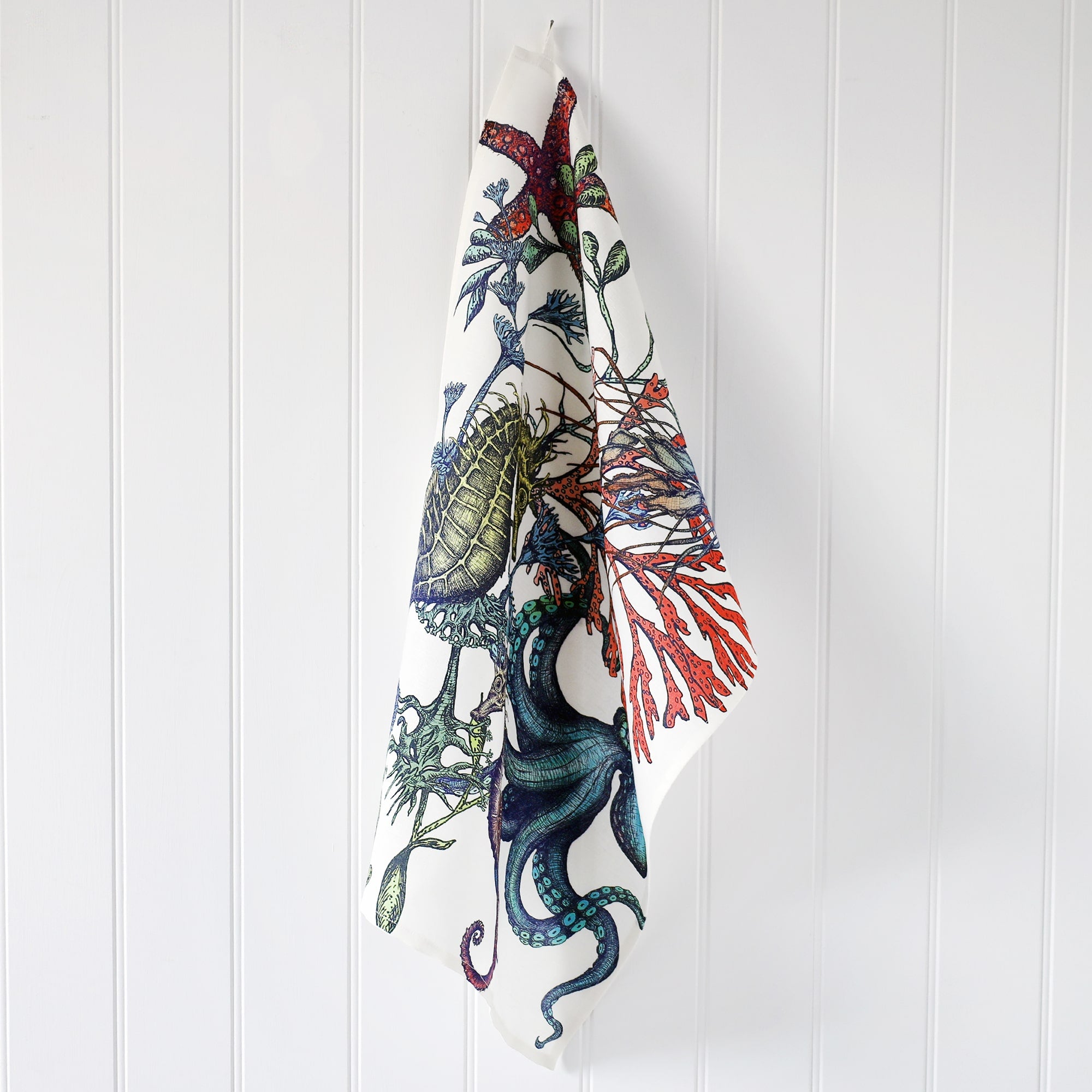 Cotton and Linen mix Tea Towel with hand drawn illustrations in Reef design with starfish,seaweed,octopus and a seahorse in various colours,hanging on a hook