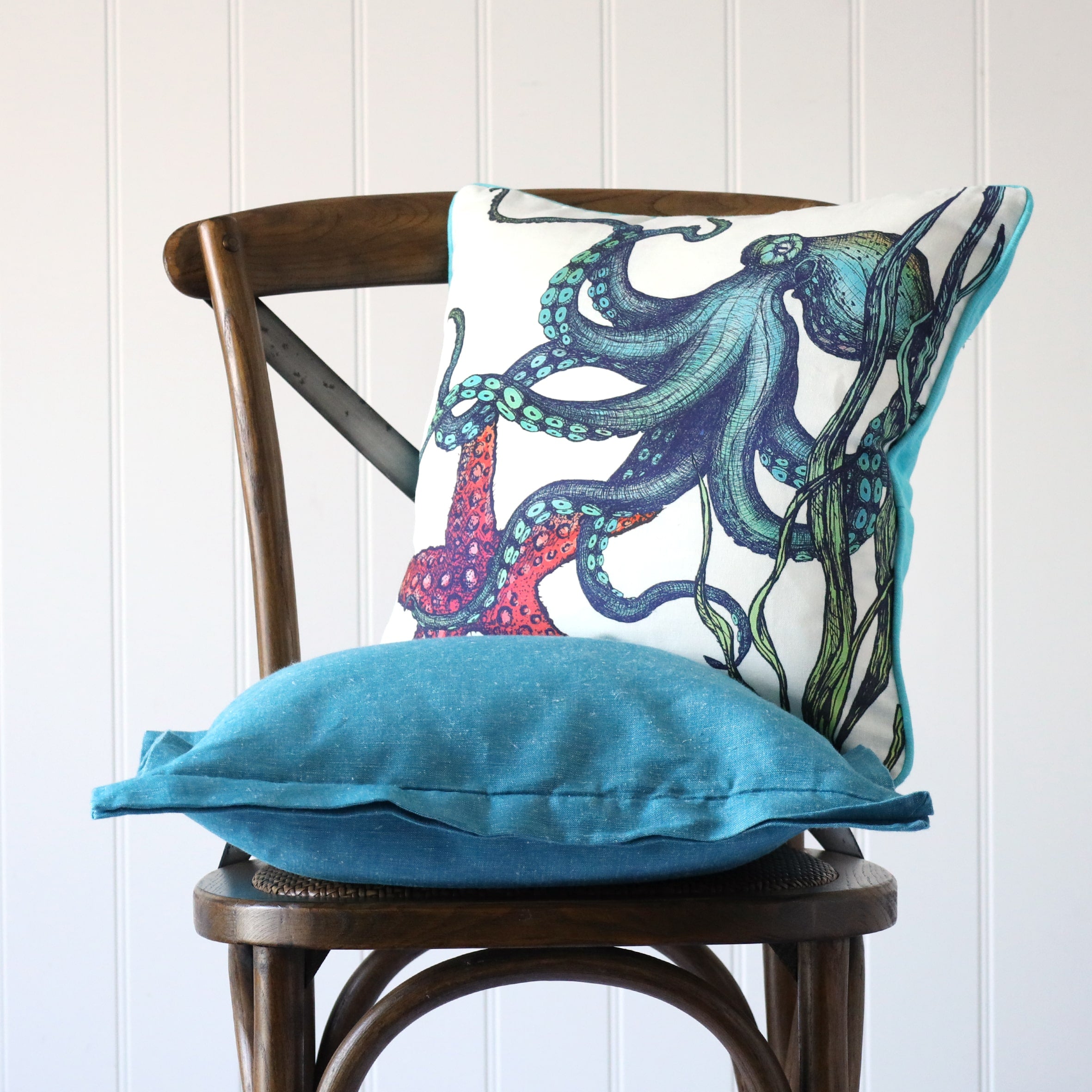 white cushion with brightly coloured illustrated of an octopus and starfish on the front, placed on a turquoise linen cushion on a wooden chair