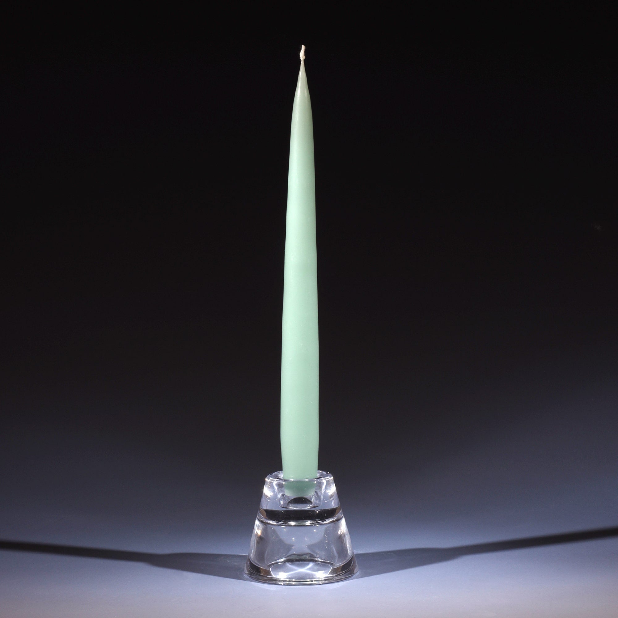 sage green tapered dinner candle in a small glass candle holder on an ombre blue background