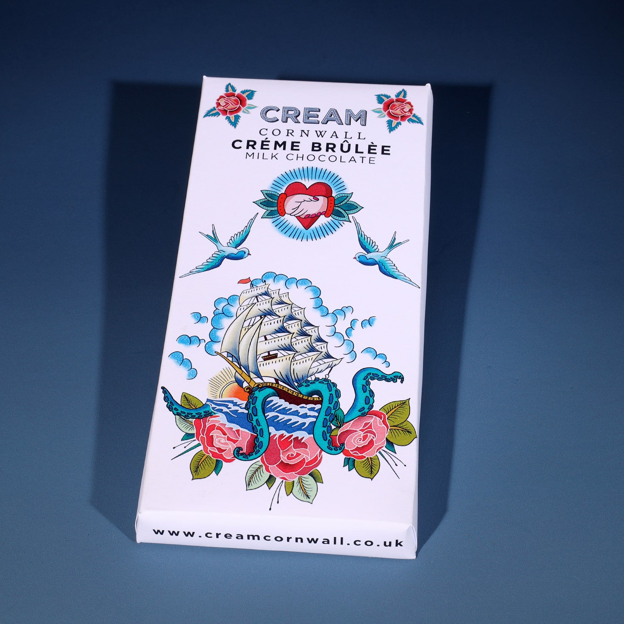 Bar of chocolate in wrapper with a ship & kraken design inspired by a sailor's tattoo, Creme Brulee flavour milk chocolate on a graduated blue background.