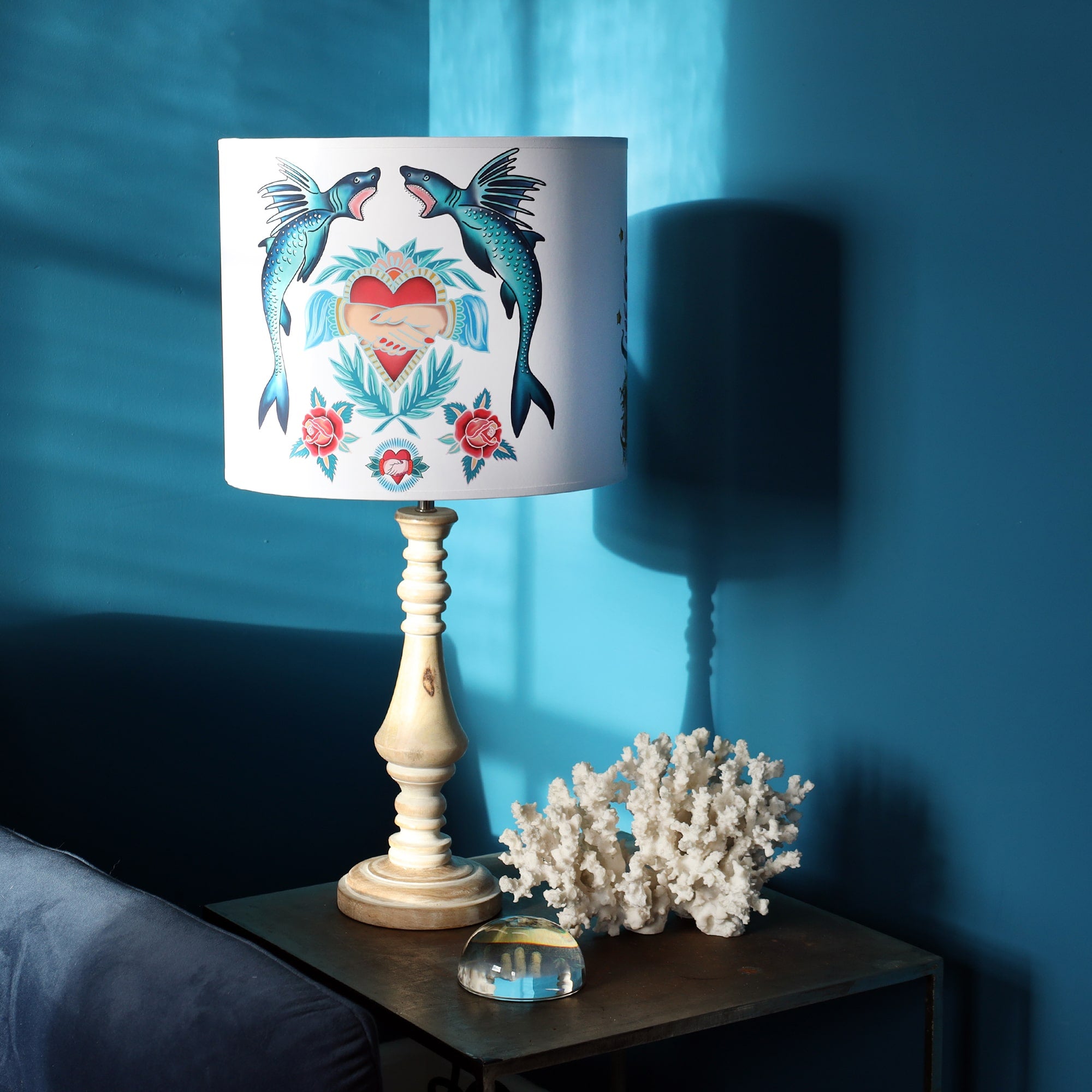 Table lamp in a teal sunny corner, the whitewashed wooden base is topped with a lampshade with sharks & hearts from our Sailor's story collection.