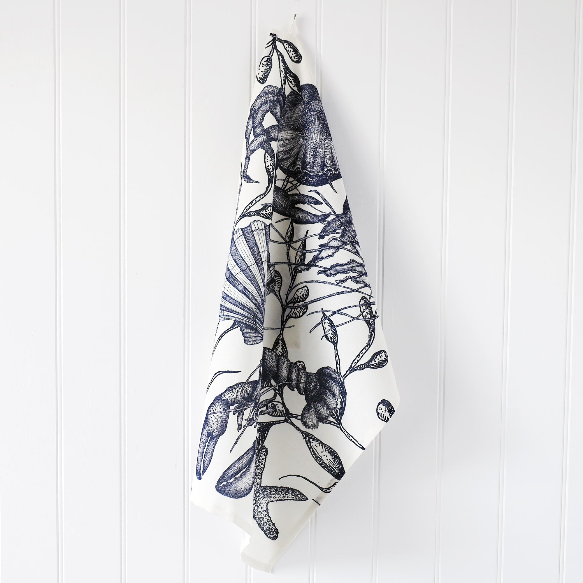 Cotton and Linen Sea Creature Tea towel decorated with hand drawn design in shades of blue on a white background,hanging from a hook