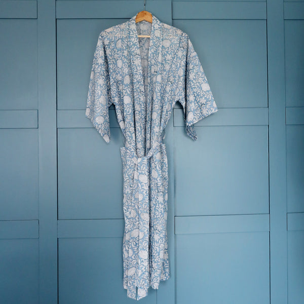 Seashell Flower dressing gown which is Hand block printed fabric  on a hanger in front of blue cupboards. 