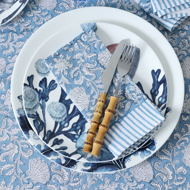  A Seashell Flower napkin on Hand block printed fabric placed on beachcomber plate and side plate.On top is a set of bamboo cutlery and all placed on a matching Hand blocked tablecloth