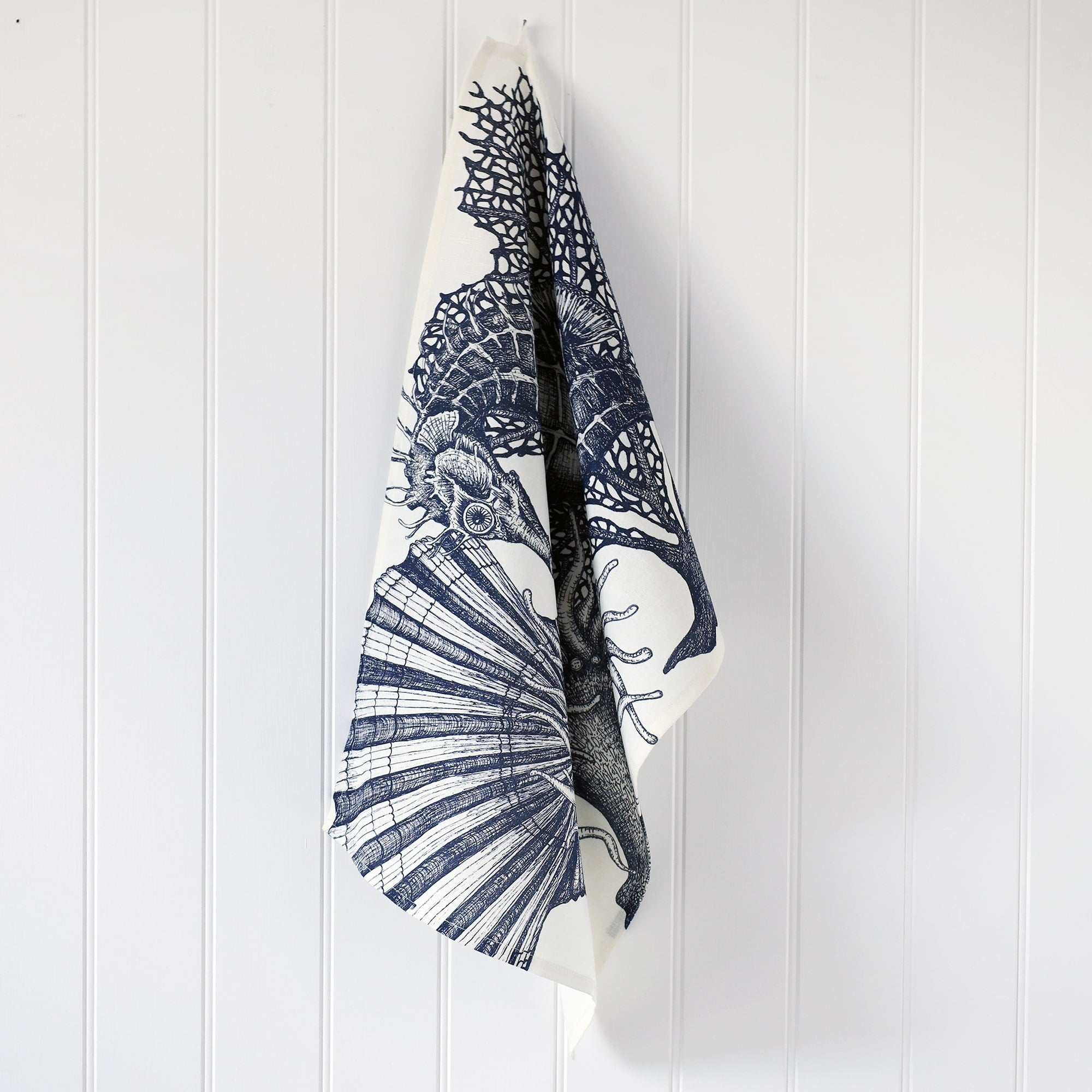Cotton and Linen Seahorse Tea towel decorated with hand drawn design in shades of blue on a white background,hanging on a hook